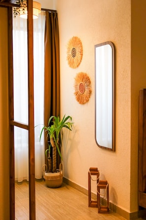 A room with a wooden floor, a potted plant, two wall-mounted decorative items, and a mirror.
