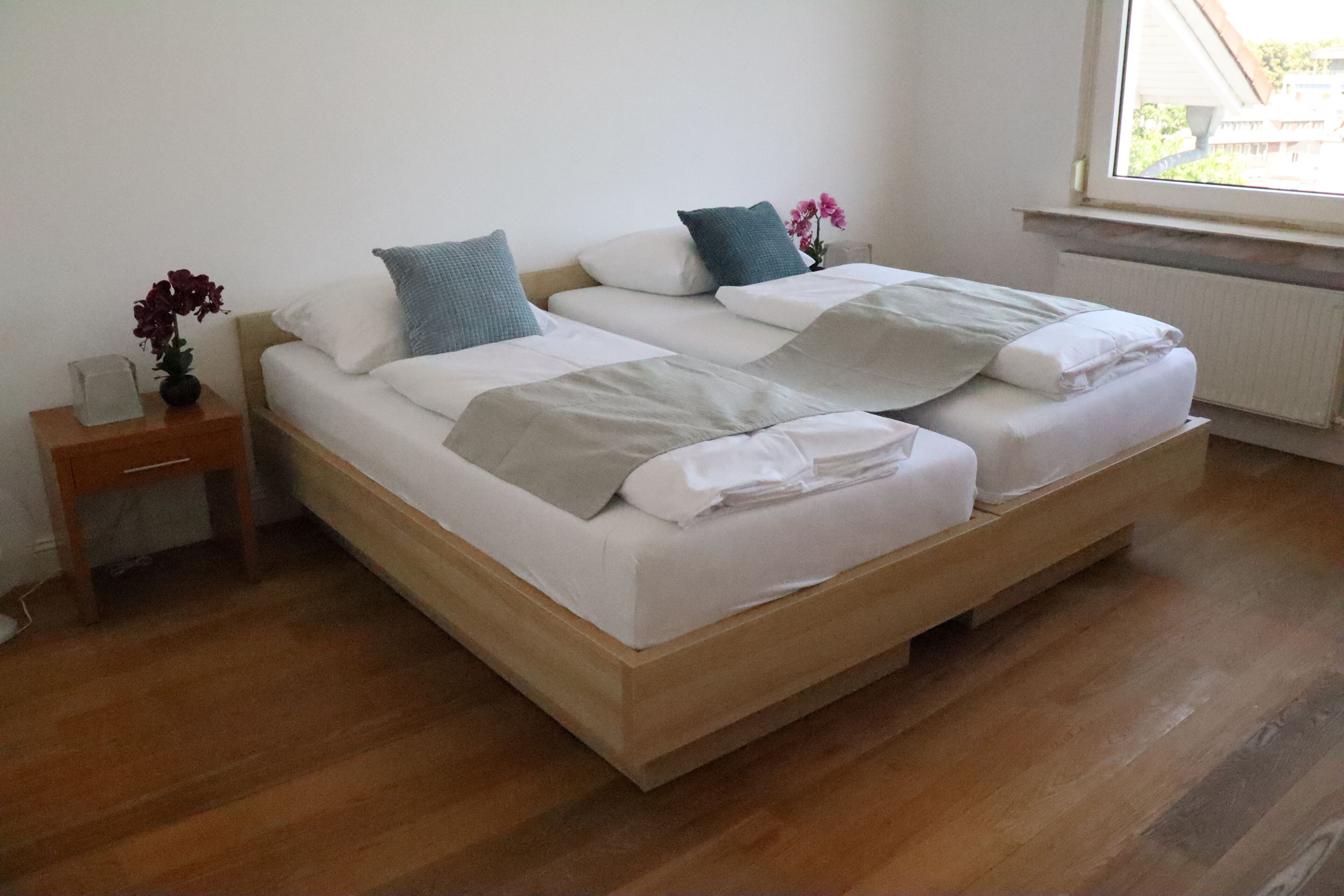 Ein Doppelbett mit Holzrahmen, weißer Bettwäsche und einem kleinen Nachttisch mit Blumen in einer Vase.