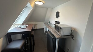 A compact kitchen with a dining area, a built-in microwave, and a wall clock. - Hotel Horstmann (Münster)