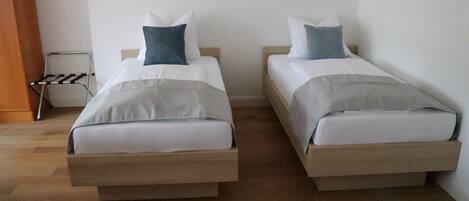 Two single beds with wooden frames and white bedding, a metal drying rack, and a wooden floor.