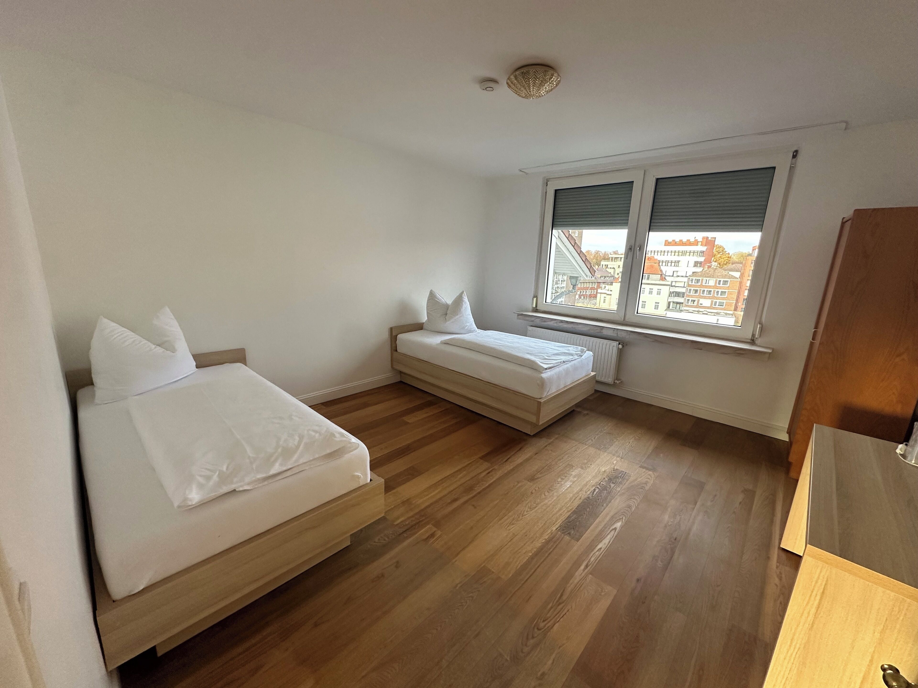 Ein kleines, sauberes Zimmer mit zwei Betten, einem Fenster mit Jalousien und einer Heizung.