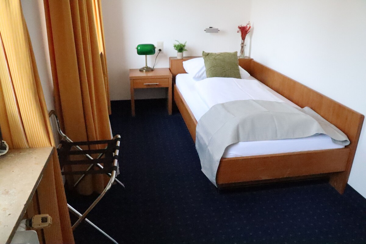 Un dormitorio pequeño y ordenado con una cama individual, una mesita de noche, un escritorio y una silla.