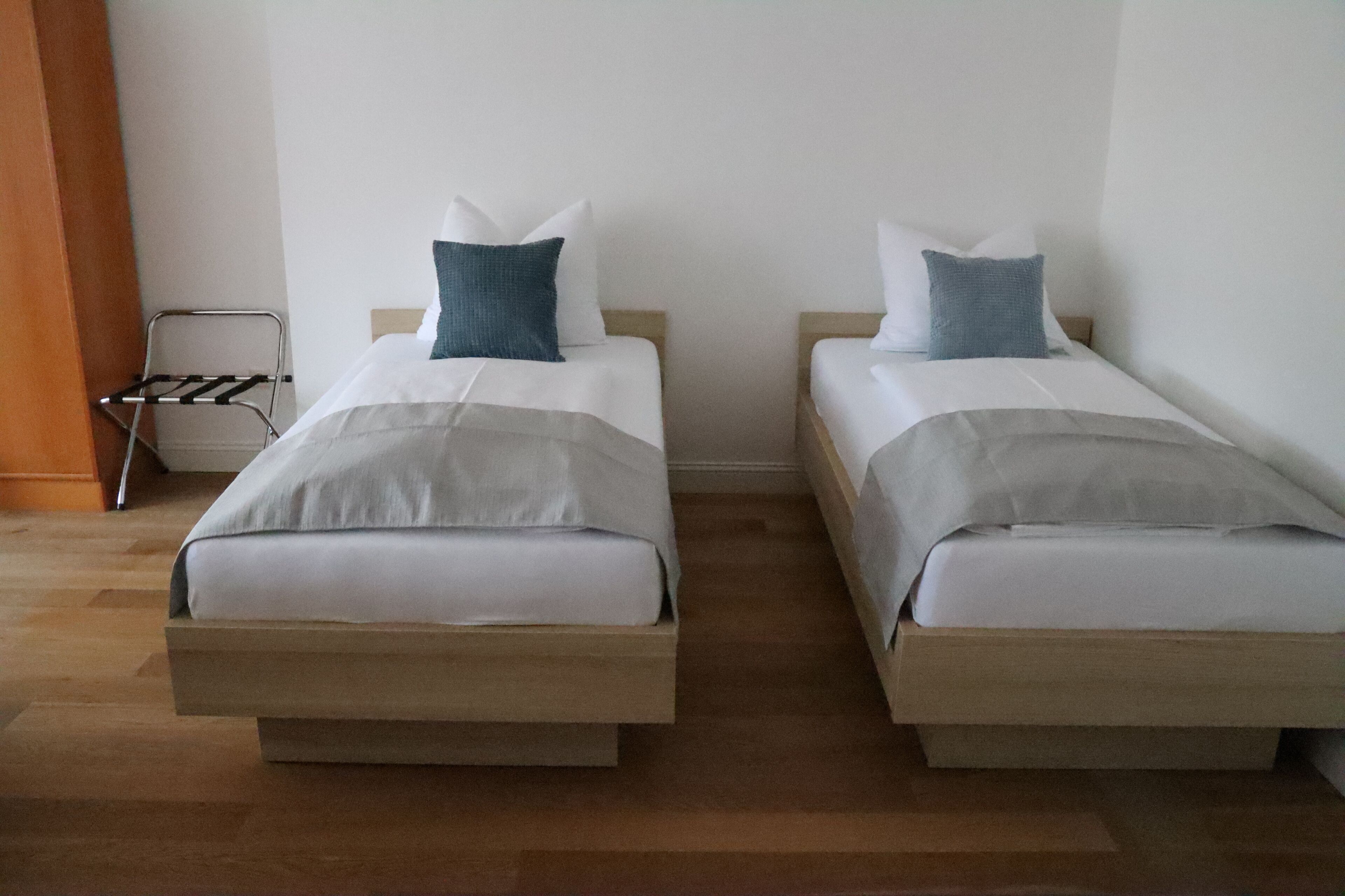 Two single beds with wooden frames and white bedding, a metal drying rack, and a wooden floor.