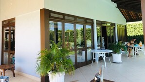 An outdoor patio area with tables and chairs, large windows, and potted plants.