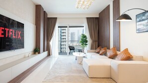A modern living room with a large flat-screen TV, a sofa set, a coffee table, and a view of the city through large windows. - KeyRock - Palm View Apt with Pool (Dubai)