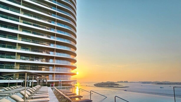 A modern hotel with a curved exterior, a rooftop infinity pool, and a sunset view. - KeyRock - Palm View Apt with Pool (Dubai)