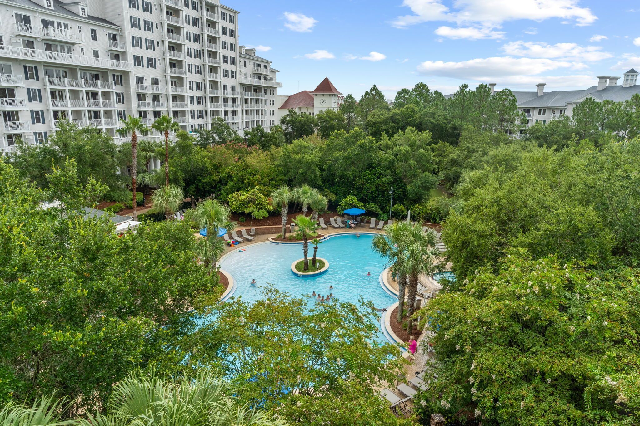 A resort with a central pool surrounded by lush greenery and a large building with multiple balconies in the background.