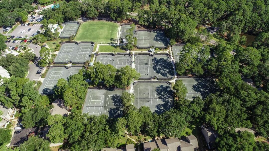 An aerial view of a residential area with multiple tennis courts surrounded by trees.