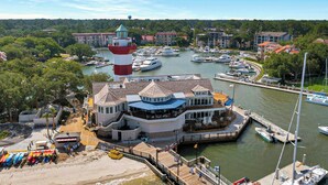 Een pand aan het water met een vuurtoren, een jachthaven en liggende boten.