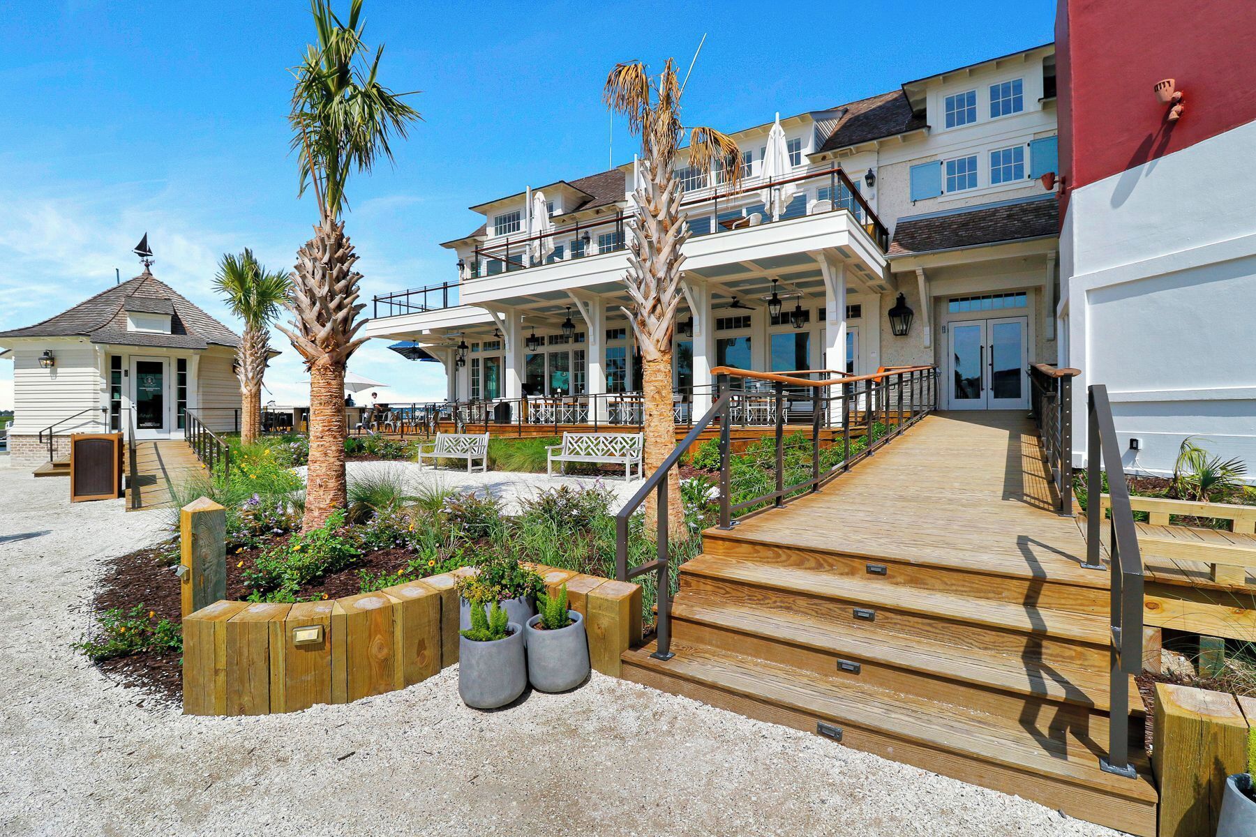 Une propriété située en bord de mer, dotée d’une terrasse en bois, d’un espace salon extérieur et d’un grand bâtiment avec de nombreuses fenêtres et balcons.