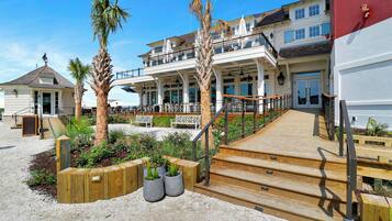 Une propriété située en bord de mer, dotée d’une terrasse en bois, d’un espace salon extérieur et d’un grand bâtiment avec de nombreuses fenêtres et balcons.