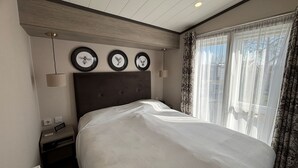 Hotelkamer met een groot bed, een hoofdeinde met drie ingelijste foto's, een bedlamp en een raam met gordijnen.