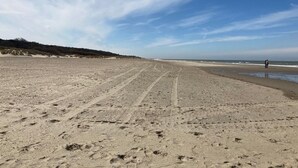 Ampia spiaggia sabbiosa con solchi di pneumatici e impronte, che si estende verso l'oceano.