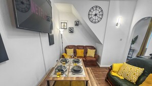 Una sala de estar moderna con una mesa de comedor preparada para cuatro personas, un sofá de cuero marrón y un plaid amarillo estampado.