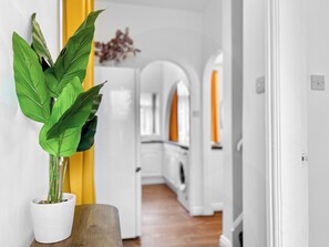 A modern kitchen with white cabinets, a wooden countertop, and a potted plant on a wooden stool.