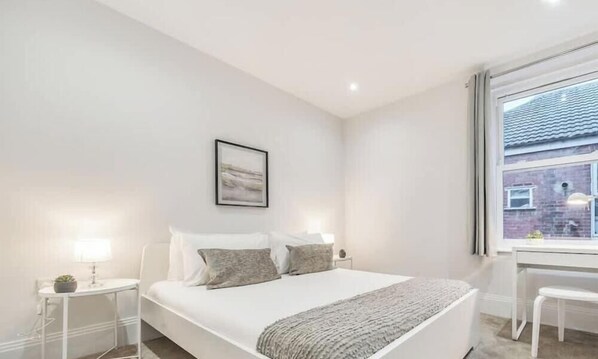 A bedroom with a bed, bedside tables, a window, and a view of a brick building.