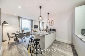 A modern kitchen with a dining area, bar stools, pendant lighting, and a view of the outdoors.