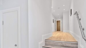 Un couloir doté d’un plancher en bois, de murs blancs et d’une rambarde métallique sur le côté droit.