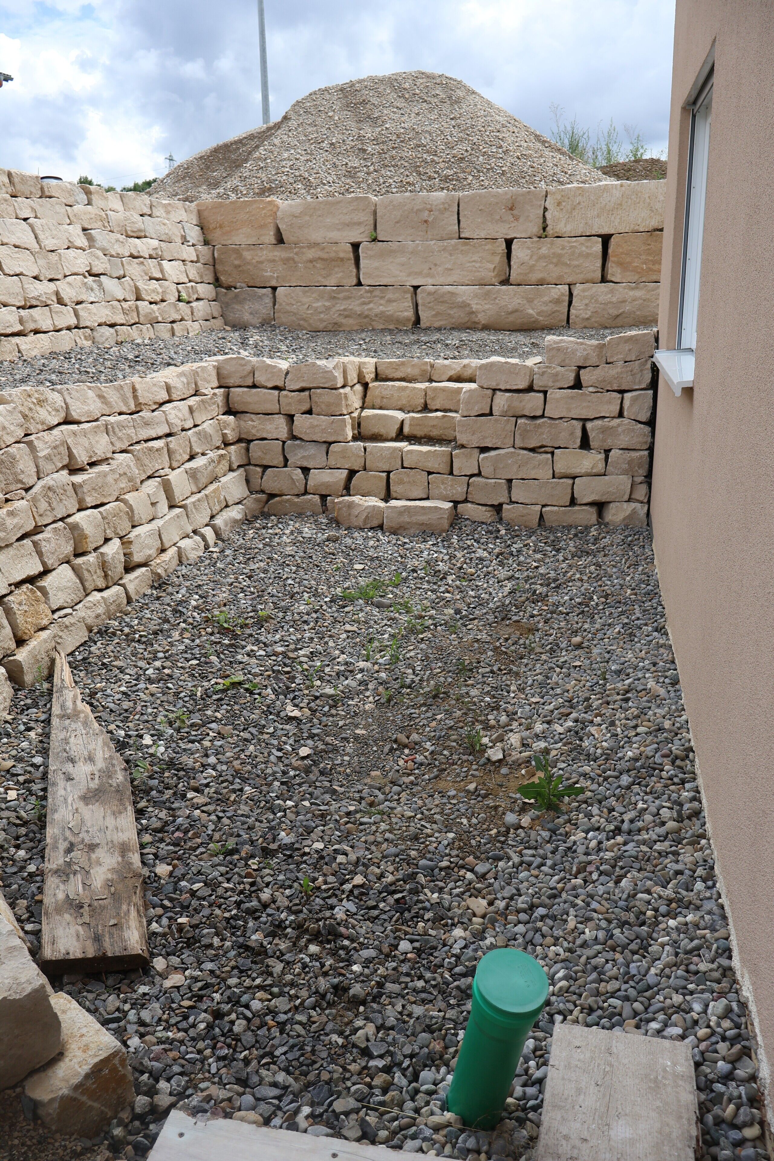 A stone wall, a gravel area, and a green cylindrical object.