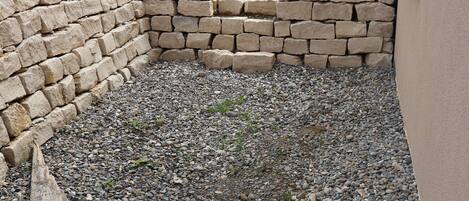 A stone wall, a gravel area, and a green cylindrical object.