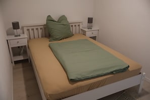A single bed with a green blanket, two bedside tables with lamps, and a white headboard. - Apartment 'Ferienwohnung Spielmann' with Wi-Fi (Sauldorf)