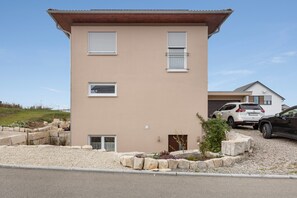 Un bâtiment à deux étages, doté d’un toit plat, d’une allée et d’un espace recouvert de gravier où sont plantées des plantes.