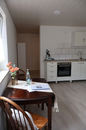 A kitchen with white cabinets, a built-in oven, and a window with flowers on the table. - Apartment 'Ferienwohnung Spielmann' with Wi-Fi (Sauldorf)