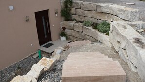 A stone pathway leading to a door, a small garden area with plants, and a stone wall.