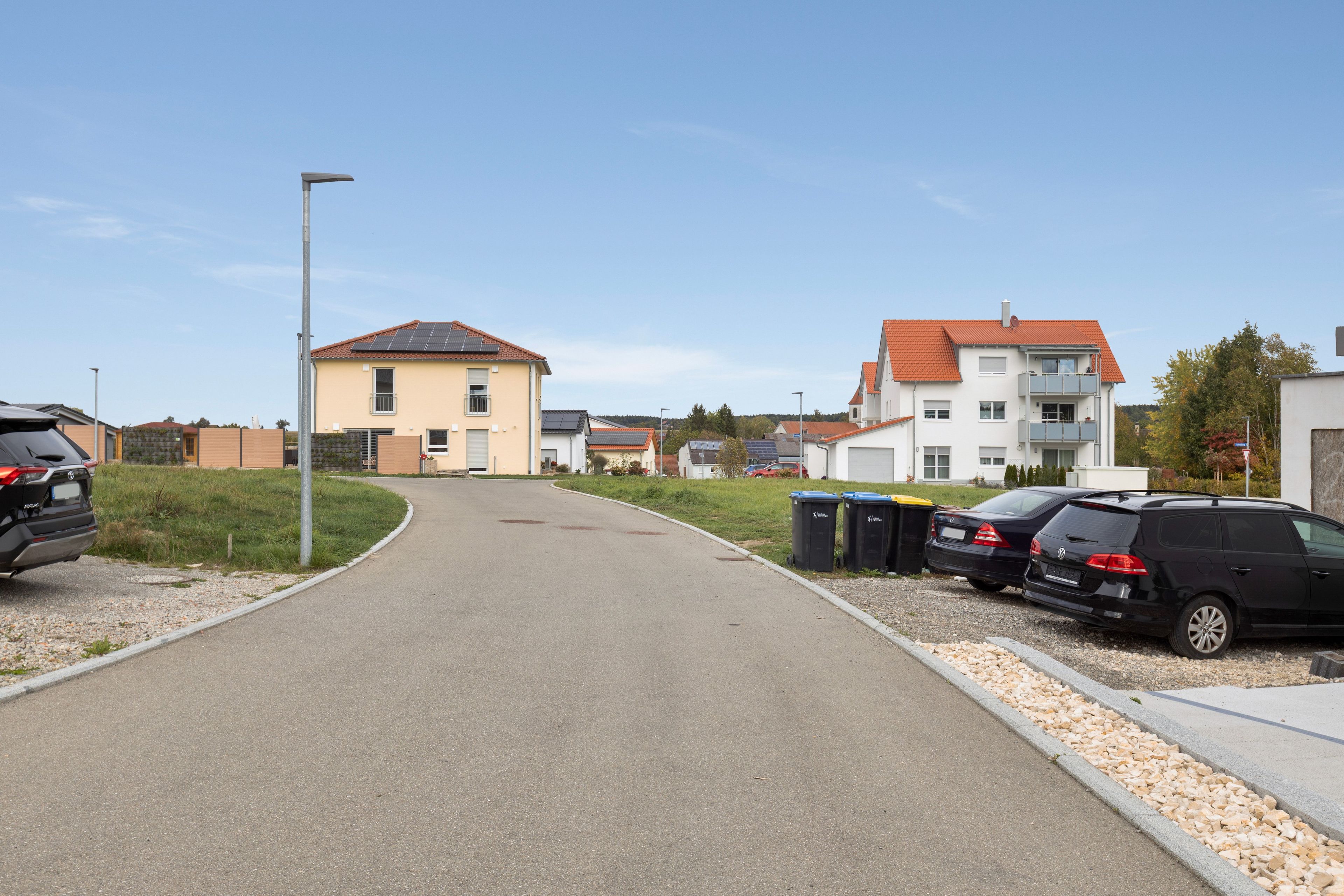 Eine Wohnstraße mit Häusern, parkenden Autos und blauem Himmel.