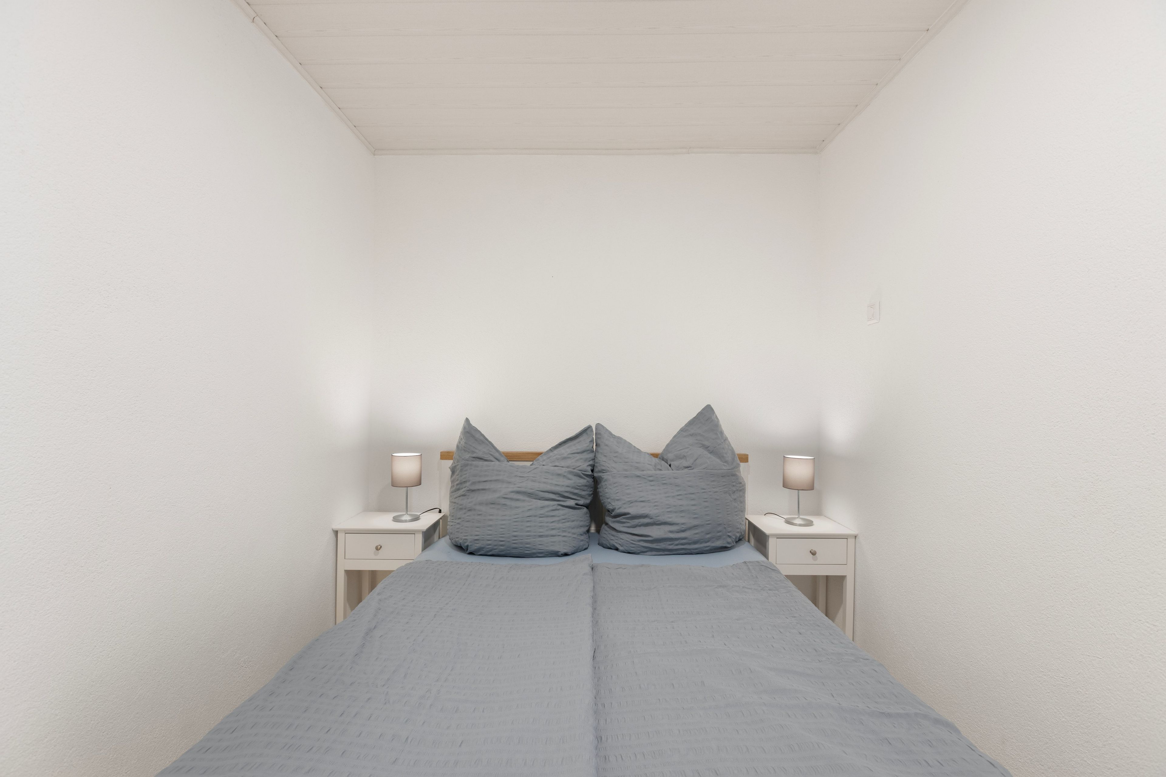 Ein kleines Zimmer mit einem Einzelbett, schrägen Wänden, zwei Nachttischen und zwei Wandleuchten.