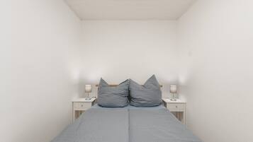 Ein kleines Zimmer mit einem Einzelbett, schrägen Wänden, zwei Nachttischen und zwei Wandleuchten.