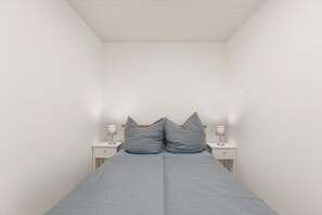 Ein kleines Zimmer mit einem Einzelbett, schrägen Wänden, zwei Nachttischen und zwei Wandleuchten.