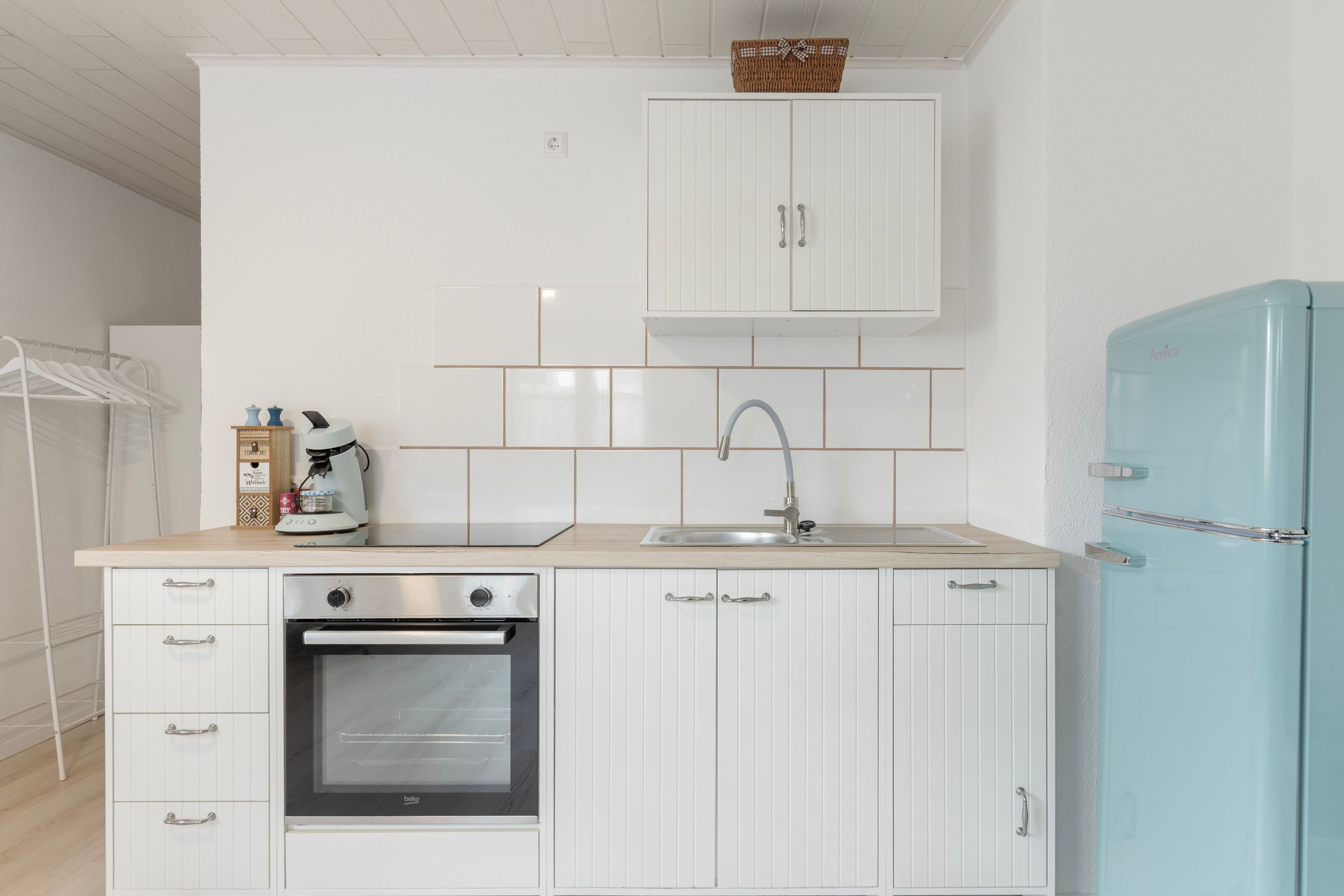 A compact kitchen with white cabinetry, a built-in oven, a sink, and a light blue refrigerator.
