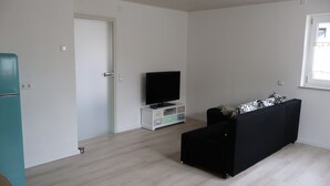 A room with a television on a white cabinet, a black sofa, and a teal refrigerator.