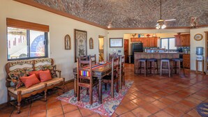 A spacious living area with a wooden dining table, a sofa with cushions, and a patterned rug. There is a kitchen area with wooden cabinets and a tiled backsplash. - Campo Bello – Rooftop Terrace, Las Conchas (Puerto Peñasco)