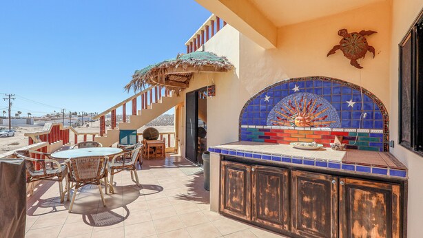A patio with wicker furniture, a tiled backsplash, and a staircase leading to an upper level. - Campo Bello – Rooftop Terrace, Las Conchas (Puerto Peñasco)