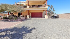 A two-story building with a red garage door, a balcony on the upper floor, and a gravel driveway. - Campo Bello – Rooftop Terrace, Las Conchas (Puerto Peñasco)