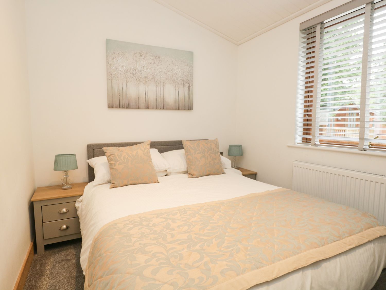 A bedroom with a bed, two bedside tables, a window with blinds, and a wall-mounted artwork.