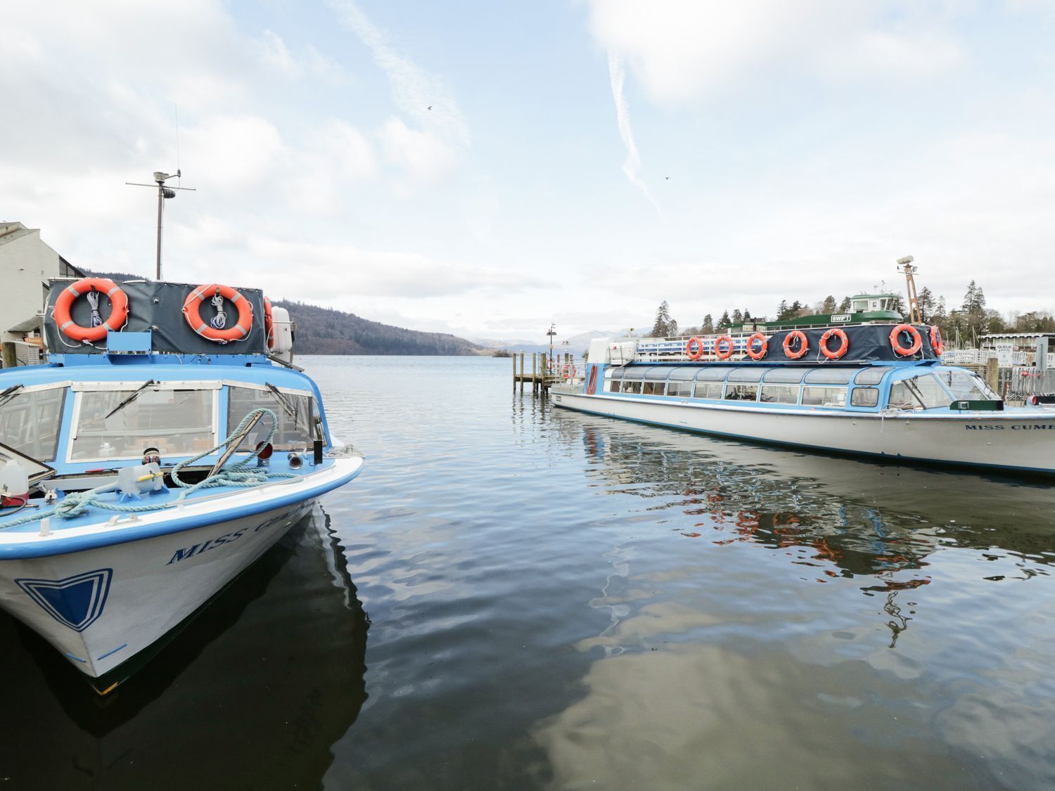 Two boats docked at a pier with lifebuoys on deck.