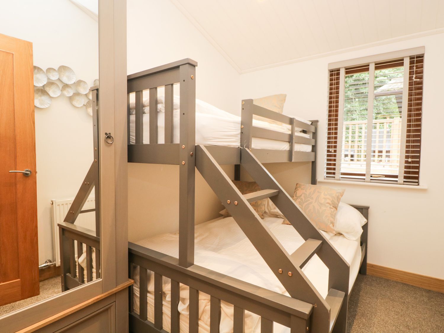 Habitación con literas, una escalera de madera, una ventana con persianas y una puerta.