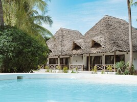 Un resort con edificios de techo de paja, piscina y vegetación tropical.
