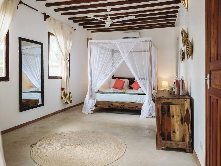 Un dormitorio con cama con dosel, una mesita de noche de madera, una alfombra tejida y un ventilador de techo.