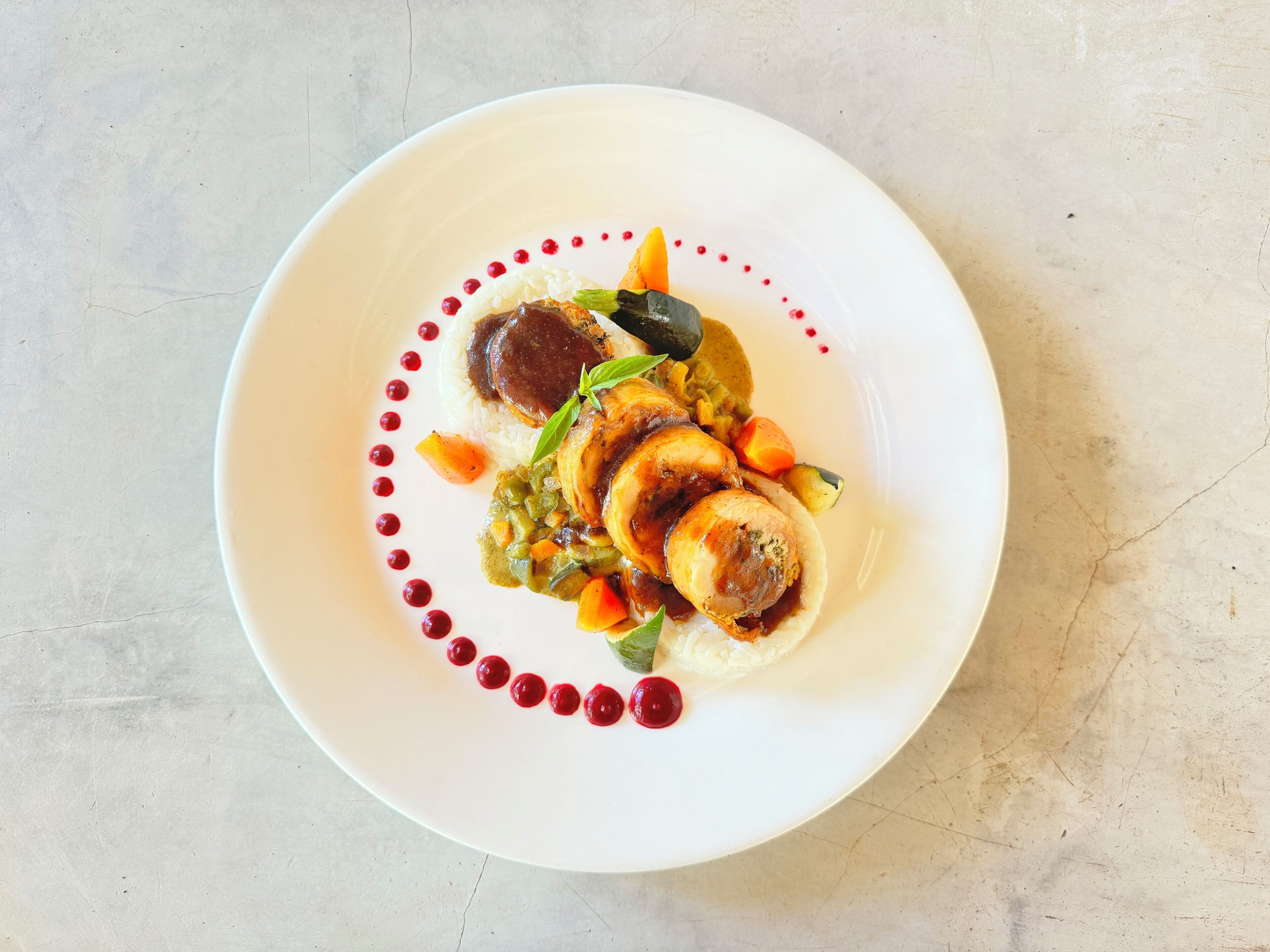 A white plate with a dish consisting of sliced meat, vegetables, and a sauce, garnished with red berries and a green leaf.