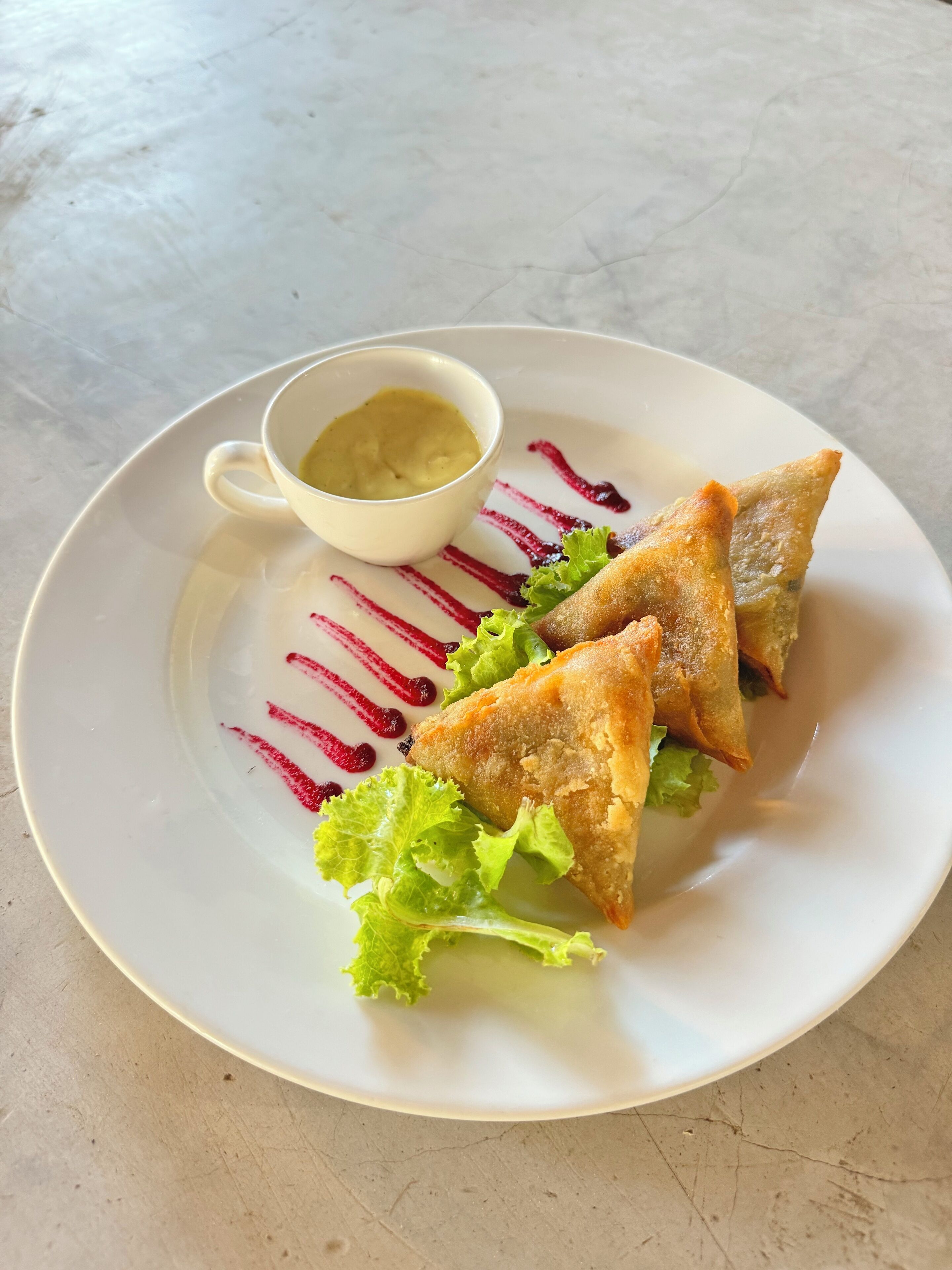 A plate with three triangular pastries, a small bowl of sauce, and some lettuce on a white plate.