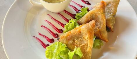 Une assiette avec trois pâtisseries triangulaires, un petit bol de sauce et quelques feuilles de laitue, le tout sur une assiette blanche.
