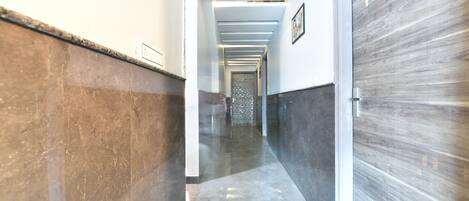 Un couloir doté d’un sol en marbre, de murs blancs et d’une porte en bois.