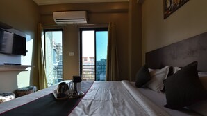 Hotelkamer met een bed, een televisie, airconditioning, een raam met gordijnen en uitzicht op de stad.