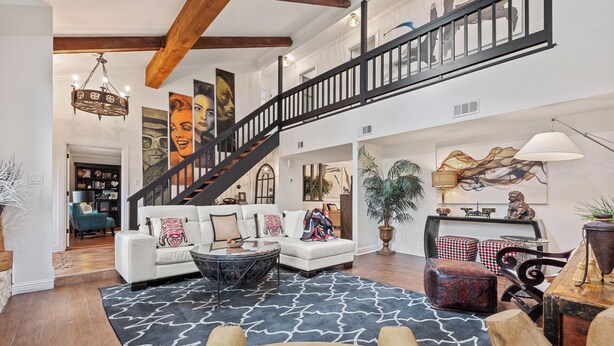 A spacious living area with a staircase, a white sofa set, a coffee table, and a large rug.