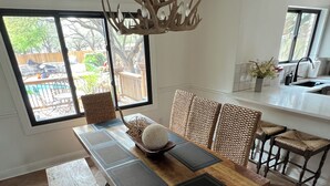 A dining area with a wooden table, woven chairs, a chandelier, and a view of the outdoors.