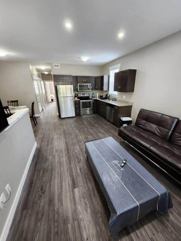 A modern living room with a dark wood floor, a leather sofa, and a covered coffee table. - Elegant Family Home by Stadium, Airport, Shopping (Regina)